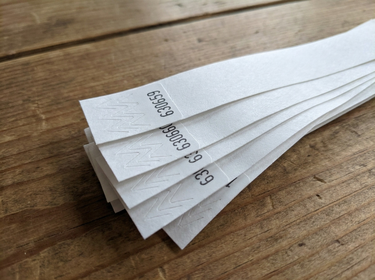 Prim-plan pe brățări Tyvek cu numerotare secvențială imprimată în negru, așezate în evantai pe o masă de control al accesului în timpul unui eveniment